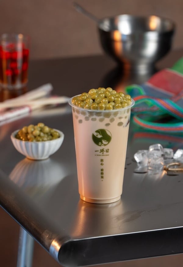 一沐日招牌逮丸奶茶，杯身旁放著草仔粿原料，強調其台灣味特色